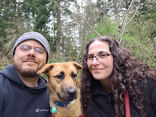 Nick, his dog and wife Leslie smiling on a hike