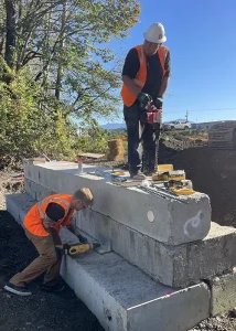 Juan standing on concrete block with saw and coworker on the ground