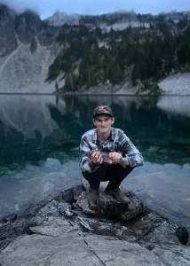Shayne poses next to lake with a fish in his hands