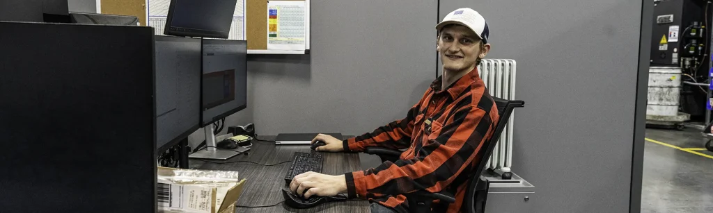 Shayne sitting at desk with NX on his desktop screen