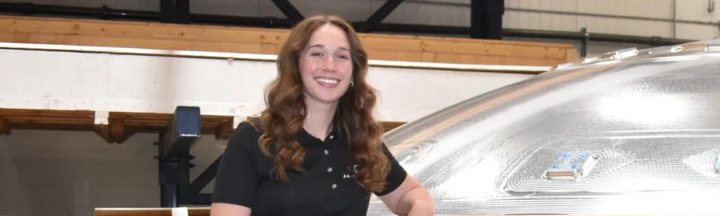 Janie, Utah engineering intern, stands next to metallic part