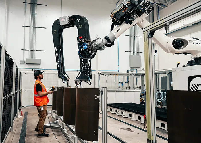 An employee stands next to an ultrasonic non destructive inspection robot and composite panels