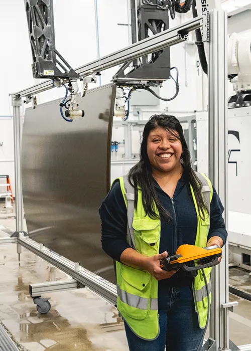 Salma, an Non Destructive Inspection role technician, stands next to a robotic arm and composite panel