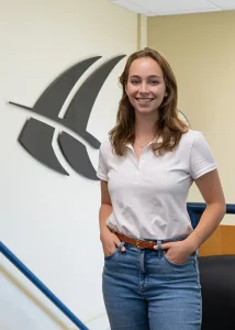 Rachel, 2025 Engineering Intern, standing in front of a carbon fiber Janicki logo