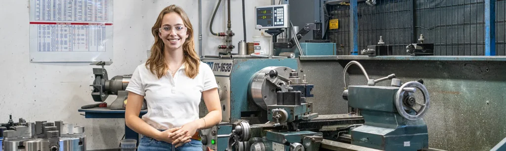 Rachel, a 2025 engineering intern, standing next to a lathe in the machine shop