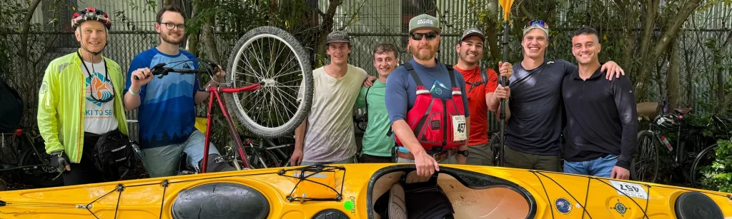 Eight members of the Janicki Pulling Left Ski to Sea team pose with their bike and kayak