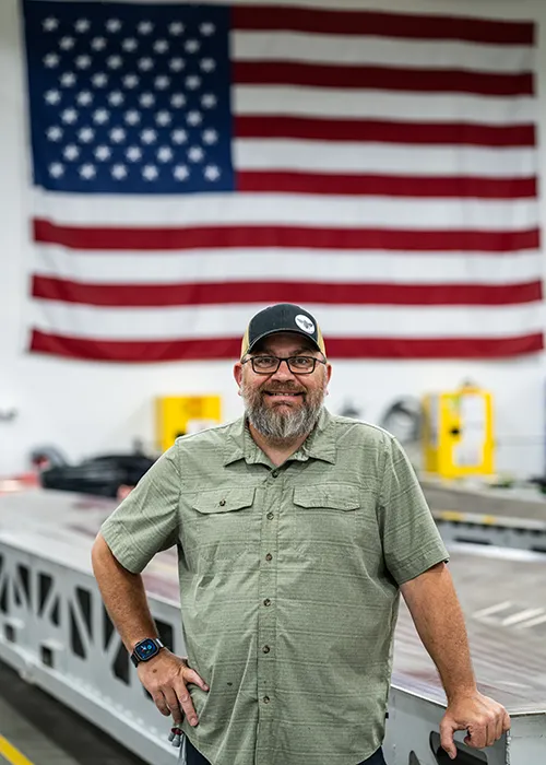 Thomas, NDI Technician, poses in front of an invar tool with a giant American flag in the background