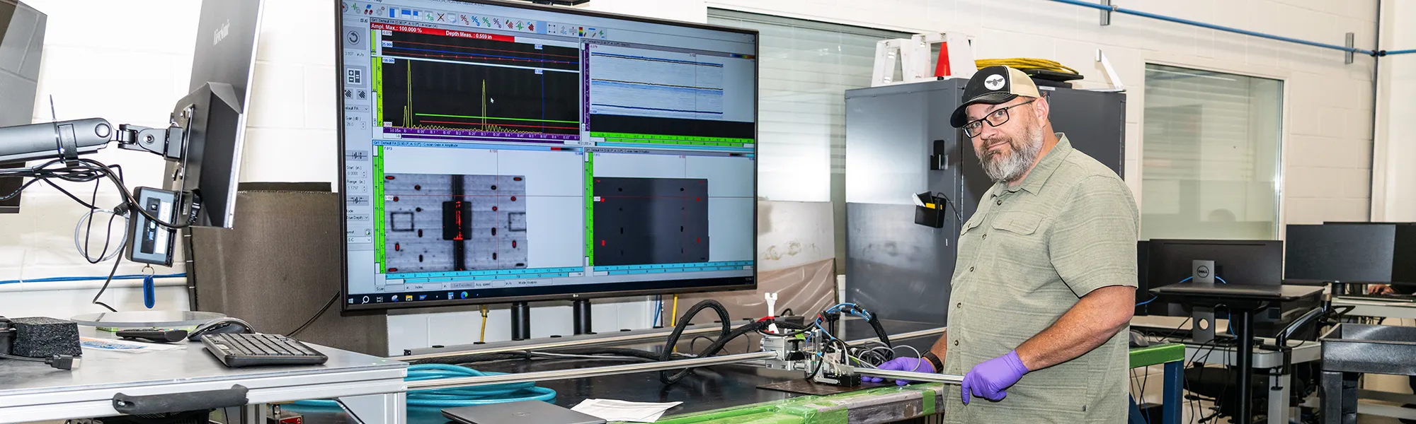 Thomas, NDI Technician, runs phased array NDI equipment. There are waves on the TV screen behind him.