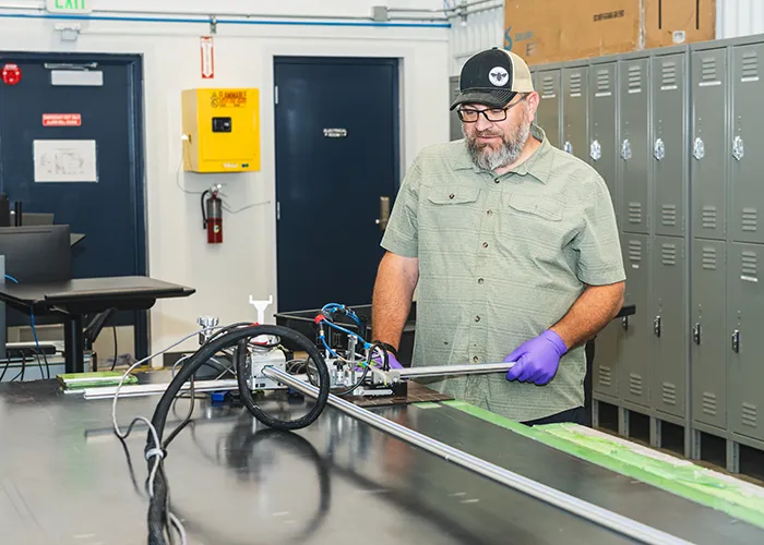 A man with a hat operates a phased array scanner to inspect a composite part