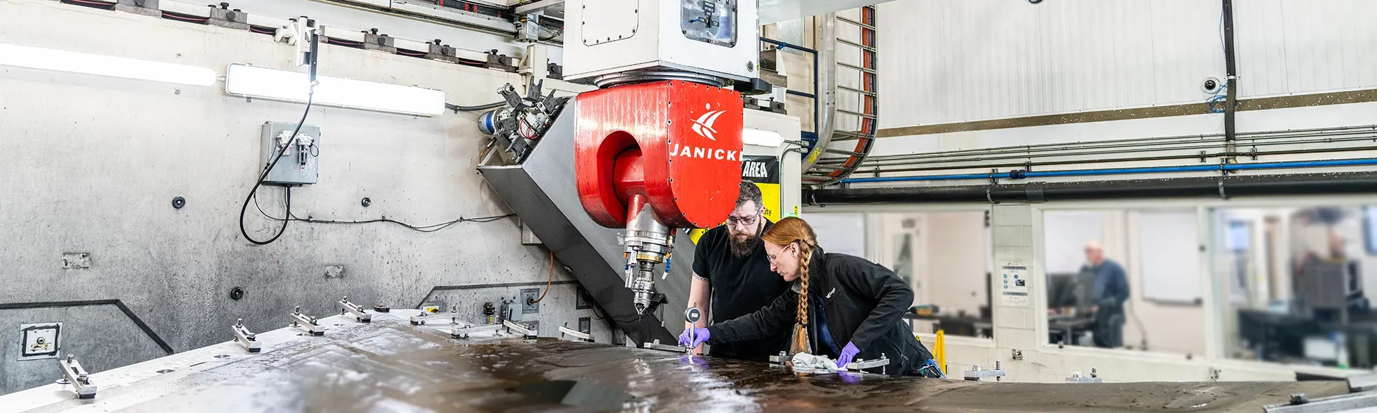 Becky, Mill Technician, works with a new tech on the mill with a composite part loaded