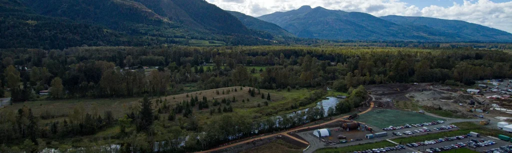 Drone view of Janicki employee park with landscaped paths, art, Carey's slough and North Cascades mountains behind the campus.