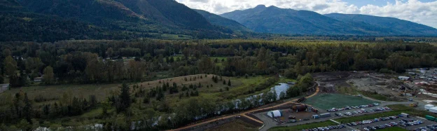 Drone view of Janicki employee park with landscaped paths, art, Carey's slough and North Cascades mountains behind the campus.