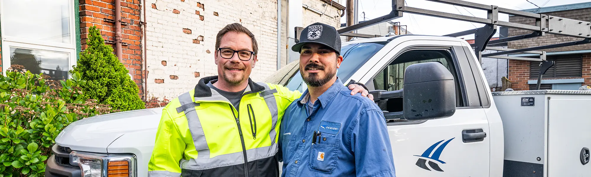 Dustin and Joe pose for a photo together in front of a Janicki facilities truck