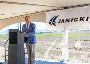 John Janicki stands at podium speaking with Janicki Industries logo behind him.