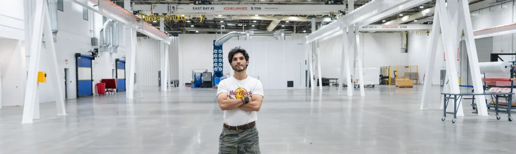 Elias, arms folded, looks at camera in manufacturing bay