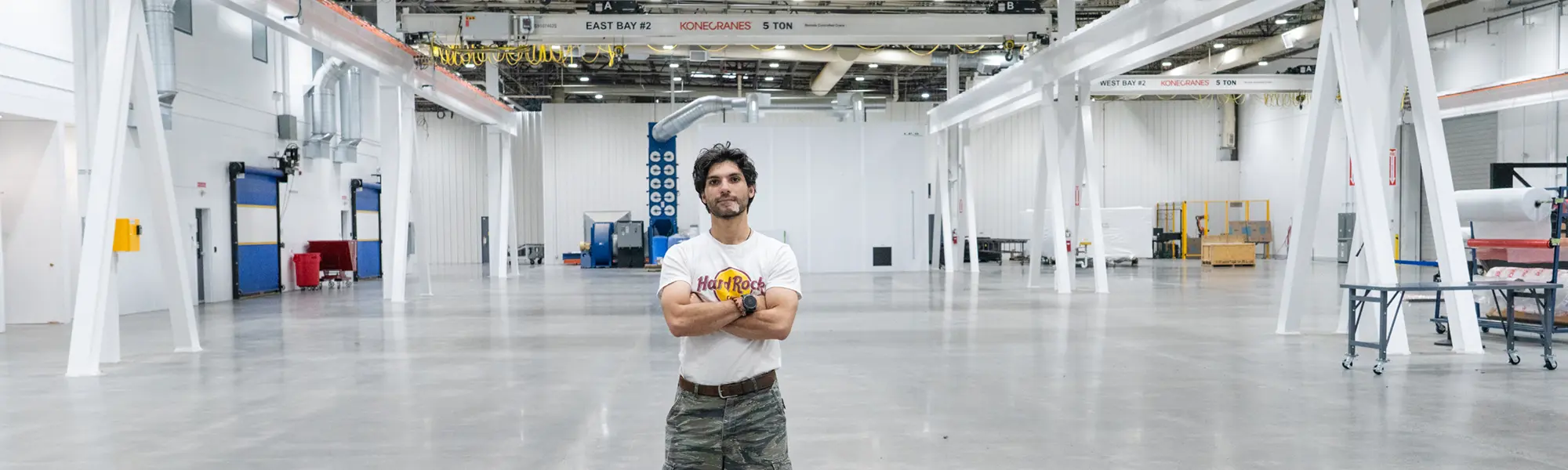 Elias, arms folded, looks at camera in manufacturing bay